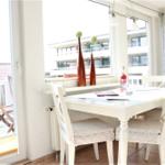 Esszimmer mit weißem Tisch und Stühlen, Blick auf Balkon und Gebäude.