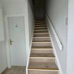 Treppenhaus mit Holztreppe und weißen Wänden. Tür mit goldenem Griff.