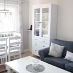 Living and dining area with sofa, table, and white chairs. Background: window with curtains.