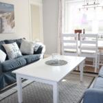 Living and dining area with sofa, table and chairs. Wall art shows beach.