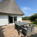Terrace with table and chairs in front of a house with thatched roof.