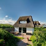 House with thatched roof, terrace, and garden. View of dunes and neighboring houses.