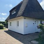 Weißes Haus mit Strohdach, Eingangstür und Blumenbeet