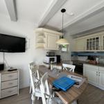 Küche mit Esstisch, weißen Schränken und TV an der Wand.