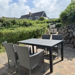 Terrasse mit Tisch und Stühlen, umgeben von Grün und Steinmauer.