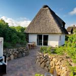 Hütte mit Strohdach, Garten, Terrasse und Strandliege.