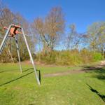 Ein Spielplatz mit Schaukel und Grünfläche unter blauem Himmel.