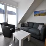 Wohnzimmer mit Sofa, Sessel und Tisch. Fenster mit Blick auf Dach. Holztreppe und Wandbild.