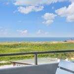 Balkon mit Blick auf das Meer und grüne Dünen.