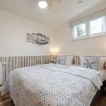 Schlafzimmer mit Bett, Nachttisch und Fenster. Wandgestaltung und Bettwäsche im Strandstil.