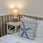 Bettkante mit Kissen und Nachttisch mit Lampe.