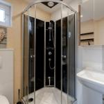 Badezimmer mit Dusche, Waschbecken und Toilette. Fenster, Spiegel und Wanddekoration sichtbar.