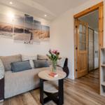 Wohnzimmer mit Sofa, Tisch und Wandbild. Holzfußboden und Tür zum Flur.