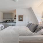 Bedroom with view of kitchen and window. Bed, table, and cabinets are visible.