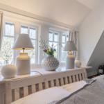 Bedroom with windows, lamps, and vase on windowsill.