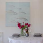 Dining table with tablecloth, two places, and wall painting with fish.
