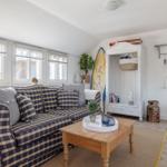 Living room with sofa, table, and wardrobe. Surfboard and plants are visible.