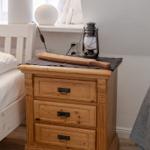 Wooden nightstand with three drawers, topped with lantern and wood piece.
