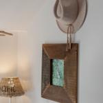 Hat hangs on wall next to wooden frame with picture and round mirror.