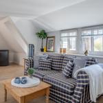 Living room with sofa, coffee table, and windows. Attic slope and wooden floor.