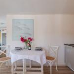Dining area with table, chairs, and kitchenette. Wall art with fish and flowers on table.