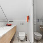 Badezimmer mit Waschbecken, Toilette und Dusche unter Dachschräge.