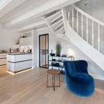 Moderne Küche mit weißen Schränken und blauer Sitzgelegenheit unter einer Treppe.