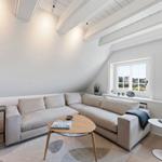 Wohnzimmer mit Ecksofa, Holztisch und Fenstern. Dachschrägen und helles Interieur.