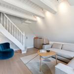 Wohnzimmer mit Sofa, blauer Sessel und weißer Treppe.