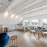 Wohn- und Essbereich mit Sofa, Tisch und Stühlen unter hohen Decken.