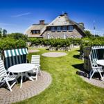 Garten mit Liegestühlen und Tischen vor einem strohgedeckten Haus.
