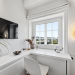 Schreibtisch mit Fensterblick, Wand-TV und Pflanze.