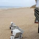 Strand mit weißen Strandkörben und Holzstegen. Blick auf den sandigen Strand und das Meer.