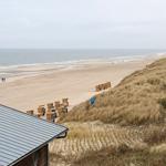 Blick auf Strand und Dünen mit Holzstühlen und Hausdach