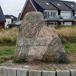 Großer Stein mit Aufschrift Wenningstedt-Braderup, Sylt, vor Wohnhäusern mit Balkonen.