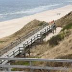 Holzsteg führt von Dünen zur Strandpromenade. Blick auf das Meer und Sandstrand.