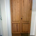 Holzschrank mit zwei Türen und schwarzen Griffen an der Wand.