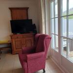 Ein Raum mit rotem Sessel, Fernseher und Fenster zur Terrasse.