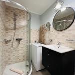 Helles und modernes Badezimmer mit großer verglaster Dusche, kostenloser Waschmaschine und Waschtischunterschrank und Kosmetikspiegel.
