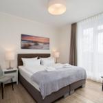 Schlafzimmer mit Bett, zwei Stühlen, Nachttischen und Wandbild.