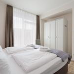 Schlafzimmer mit Bett, Kleiderschrank und Fenster mit Vorhängen.