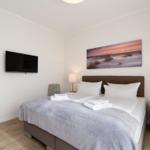 Schlafzimmer mit Doppelbett, Wandbild, Nachttisch und Fernseher.