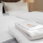 Bett mit weißen Laken und gefalteten Handtüchern mit Logo.