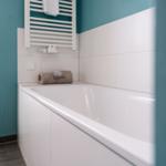 Bad mit Badewanne, Duschwand und Fenster mit Jalousie.