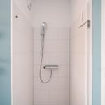 Dusche mit Handbrause und Chromarmaturen an blauer Wand