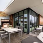 Terrasse mit Sitzgruppe, Tisch, Sonnenschirm und Grill. Große Glasfront zum Eingang.
