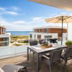 Terrasse mit Tisch, Stühlen und Sonnenschirm. Blick auf das Meer und moderne Gebäude.
