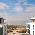 Zwei moderne Gebäude flankieren einen Blick aufs Meer und einen Spielplatz.