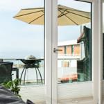 Durch die Glastür ist eine Terrasse mit Grill und Sonnenschirm zu sehen.