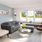 Wohnzimmer mit grauem Sofa, braunem Sessel und Glas-Tisch.